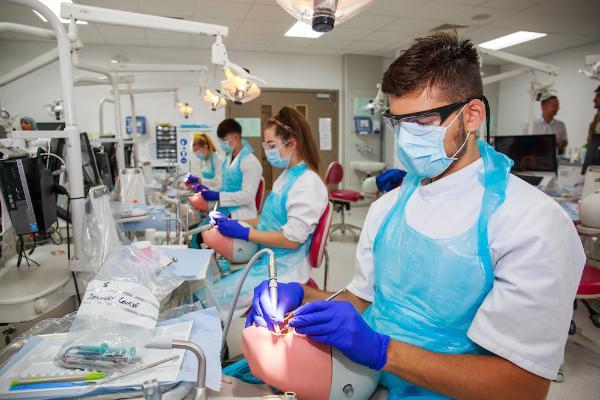 Four dental students in masks and aprons practising on models