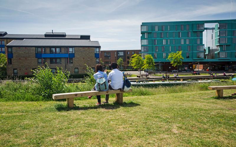 Two people sitting on a bench in Mile End Park looking across the canal towards Queen Mary campus