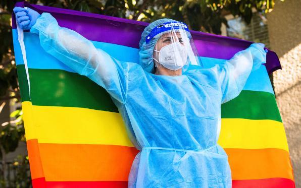 Female Healthcare worker wearing a protective face mask and a face shield holding a gay flag looking up