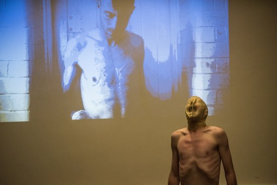 O'Brien performs wearing a latex mask as an image of himself is projected on the back wall