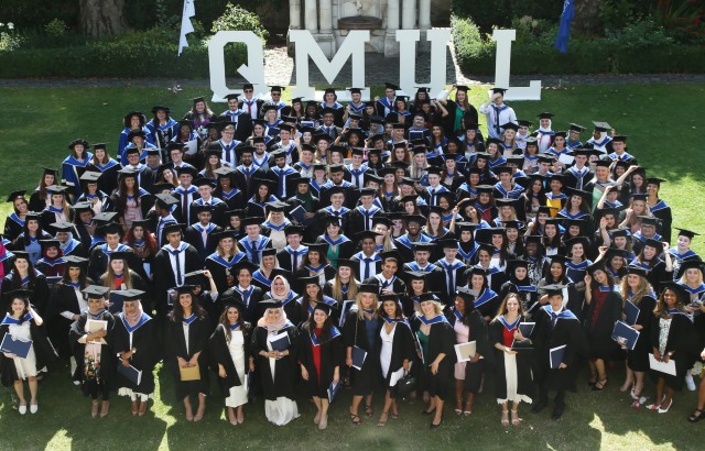 Large group of graduands with QMUL letters in background.