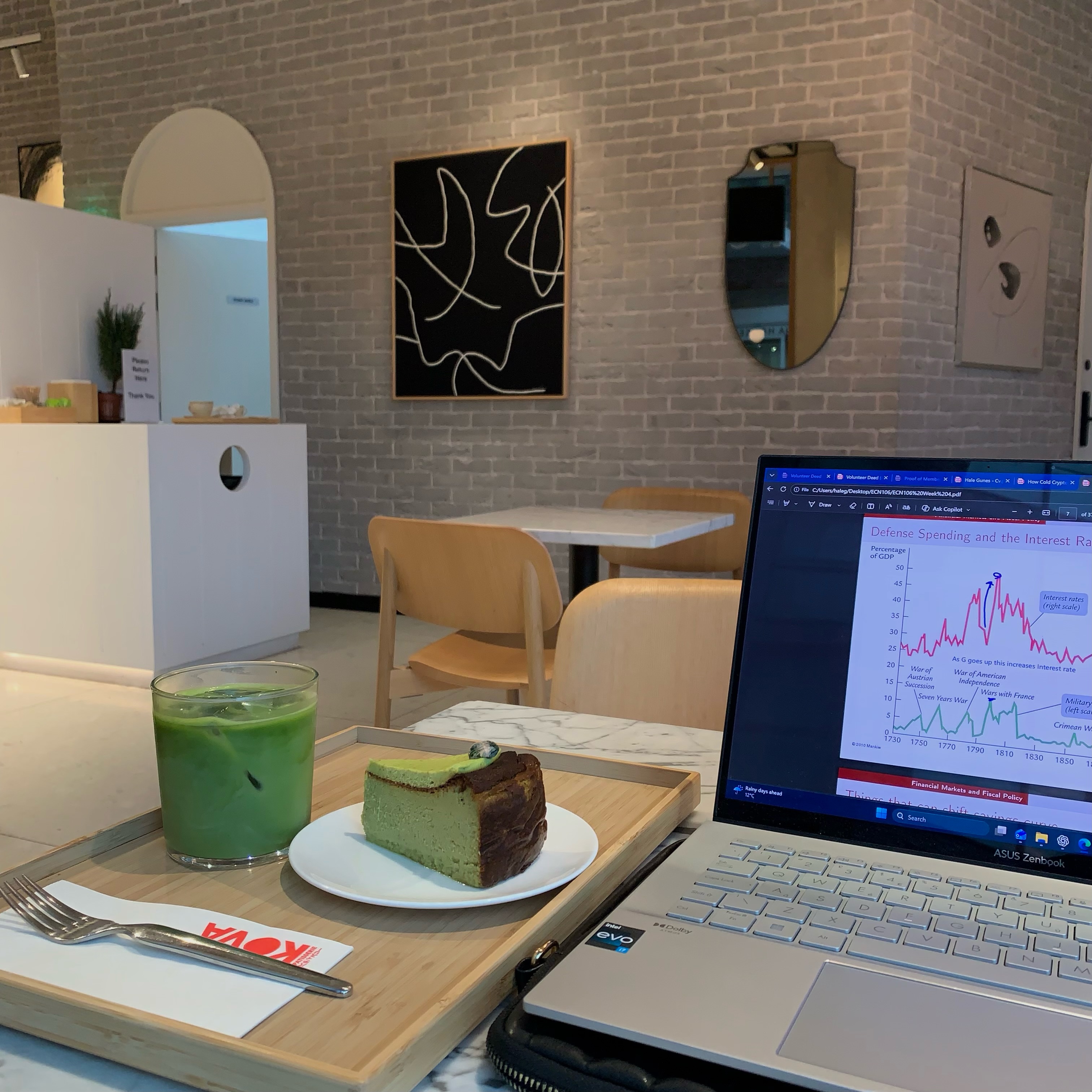 An image inside a cafe, a cake, tea and a laptop is on a table