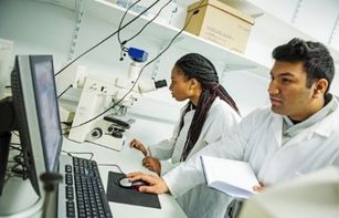 Two researchers conducting research in a lab using a microscope and a computer