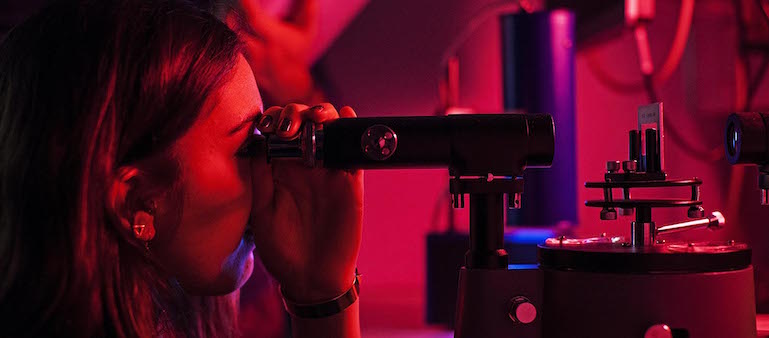 Image of student looking through a microscope during an experiment.