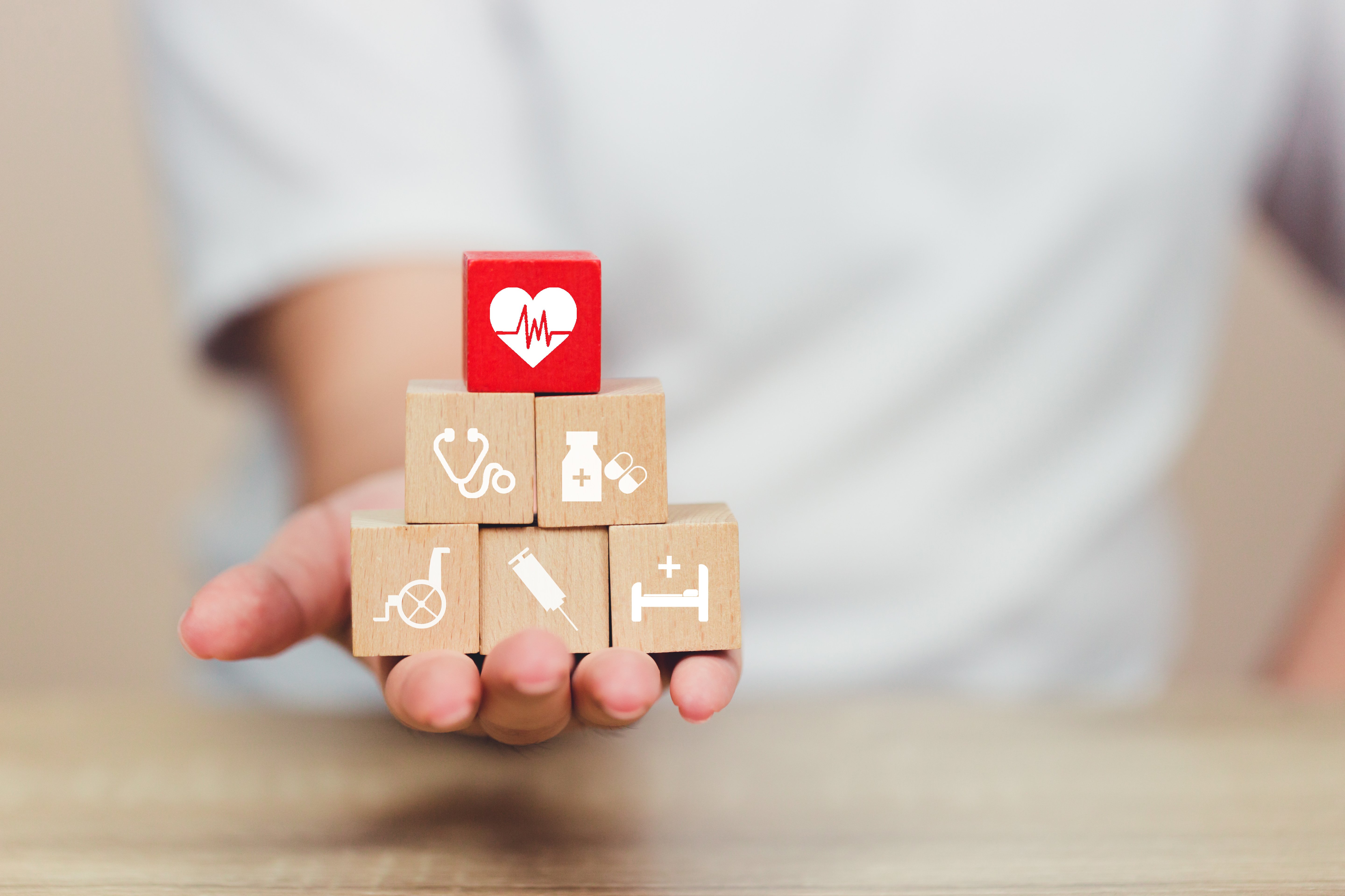 A hand holding wooden blocks with medical symbols, topped with a red block featuring a heart