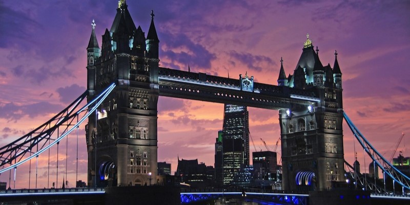 A photo showing Tower Bridge at night with a purple sky and lights from the surrounding buildings.