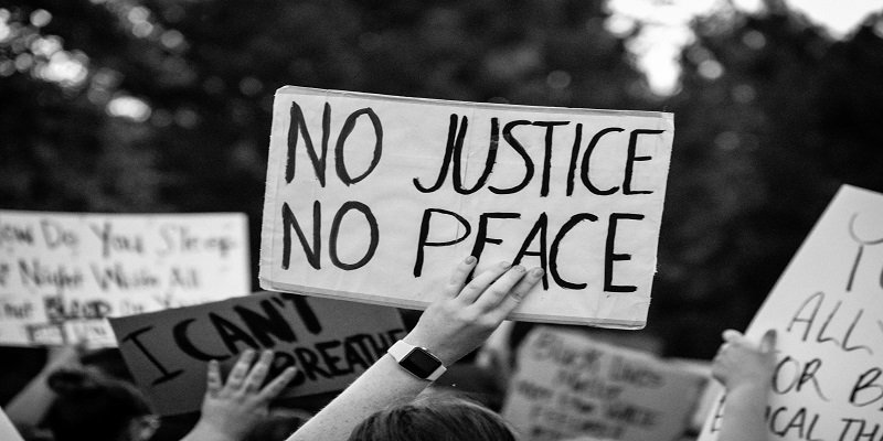the hand of a person at a protest holding a sign staying No Justice, No Peace