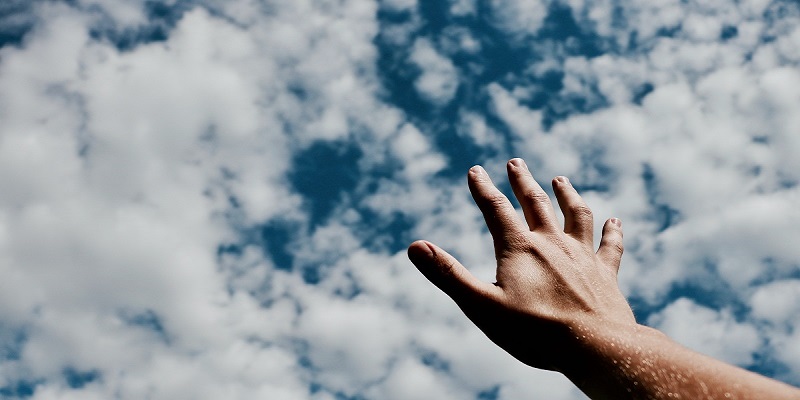 a human hand reaching towards a blue sky