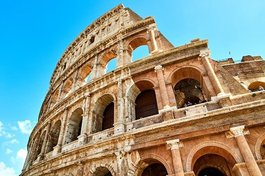 a picture of part of the Colosseum in Rome with a bright blue sky behind it