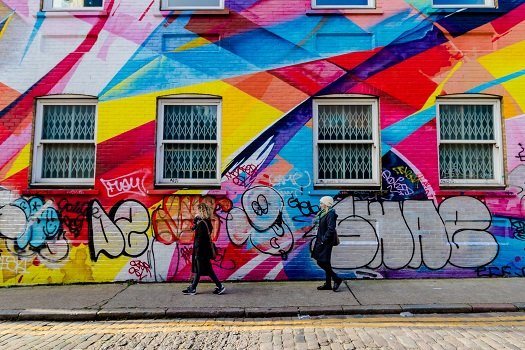 People walking past a wall in the East End that has been brightly decorated with different coloured paints