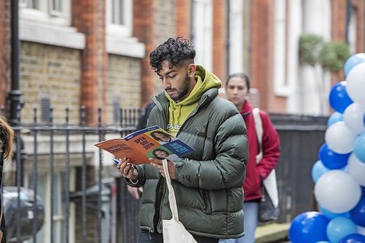 a young man on Queen Mary's Mile End Campus reading a book