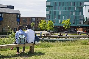 students sitting on a bench look at Regents Canal from the Mile End Campus of Queen Mary University