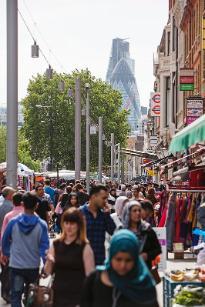 A busy street with crowds at Whitechapel market looking towards The City of London