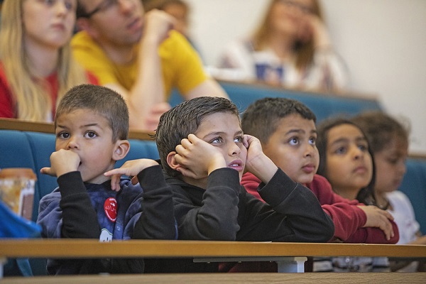 Four young children in a lecture theatre listening to a talk at QMUL's Festival of Communities