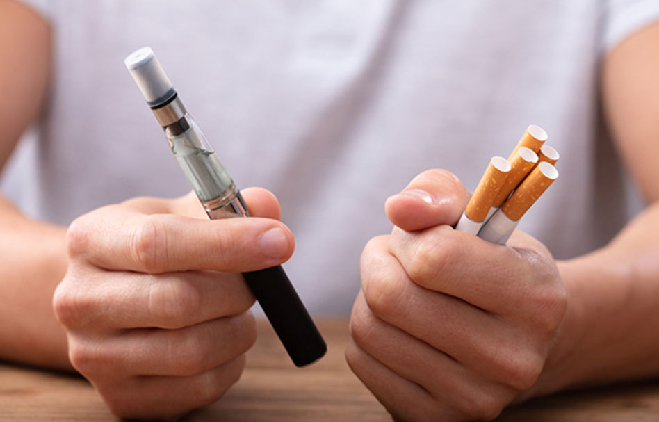 A person holding a vape on one hand and cigarettes on the other hand