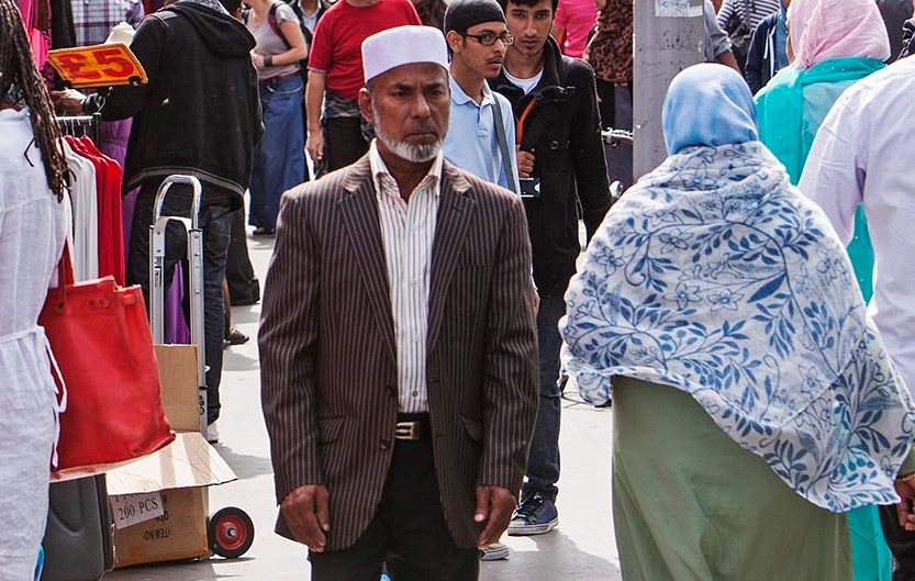 A man of South Asian background walks through a market in the East End of London