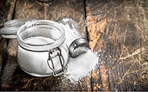 A salt shaker and a jar of salt on a wooden table